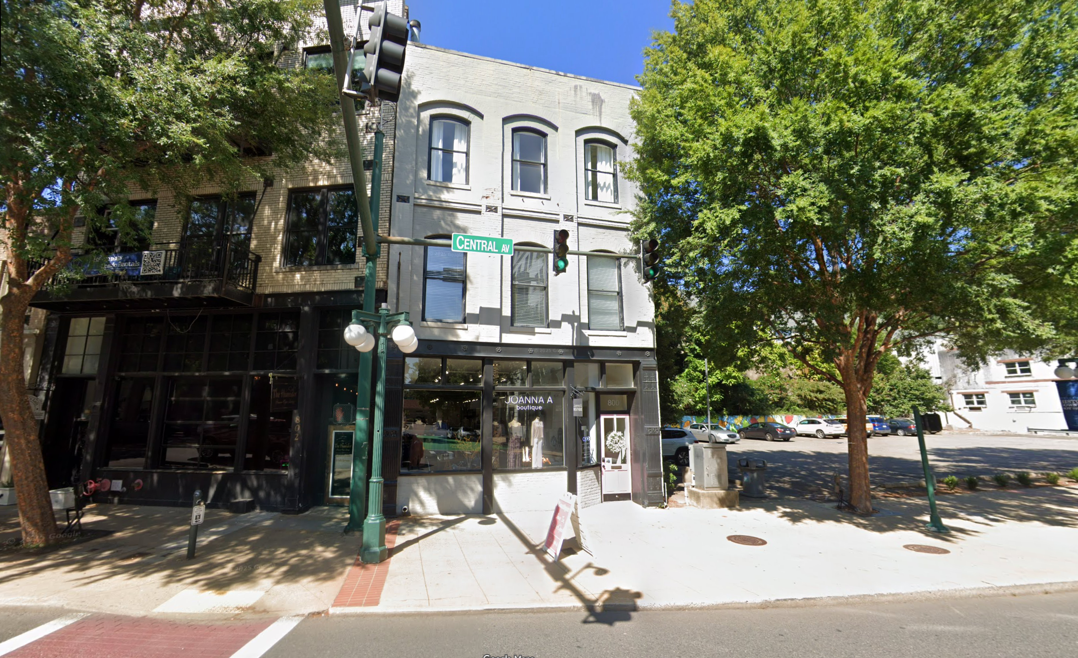 Street view of a multi-story building with storefronts on a sunny day.